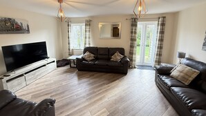 A living room with a large flat-screen TV, two leather sofas, a coffee table, and a wooden floor. - Stunning Coastal Cottage - Sleeping 6 in 3 Bedrooms - Pool and Beach Access Included. (Filey)
