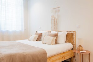 Un dormitorio con una cama de madera, ropa de cama blanca, una mesita de noche con una lámpara y un cuadro colgado en la pared.