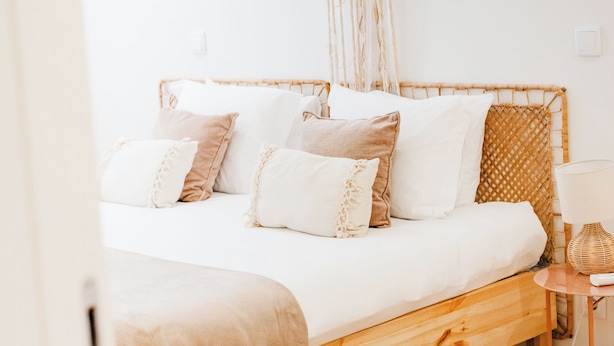 Uma cama com estrutura de madeira, roupa de cama branca e um abajur.