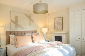 A bedroom with a large bed, bedside lamps, a fireplace, and a door. - Park Cottage (Glaston)