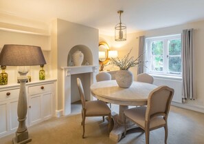 A dining area with a round table, four chairs, a lamp, a vase, and a fireplace. - Park Cottage (Glaston)