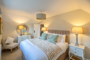 A bedroom with a large bed, two bedside tables with lamps, a chair, and a round mirror. - Park Cottage (Glaston)