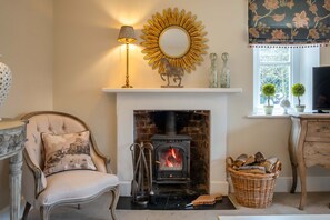 A cozy living room with a fireplace, a comfortable armchair, a lamp, and a decorative mirror. - Park Cottage (Glaston)