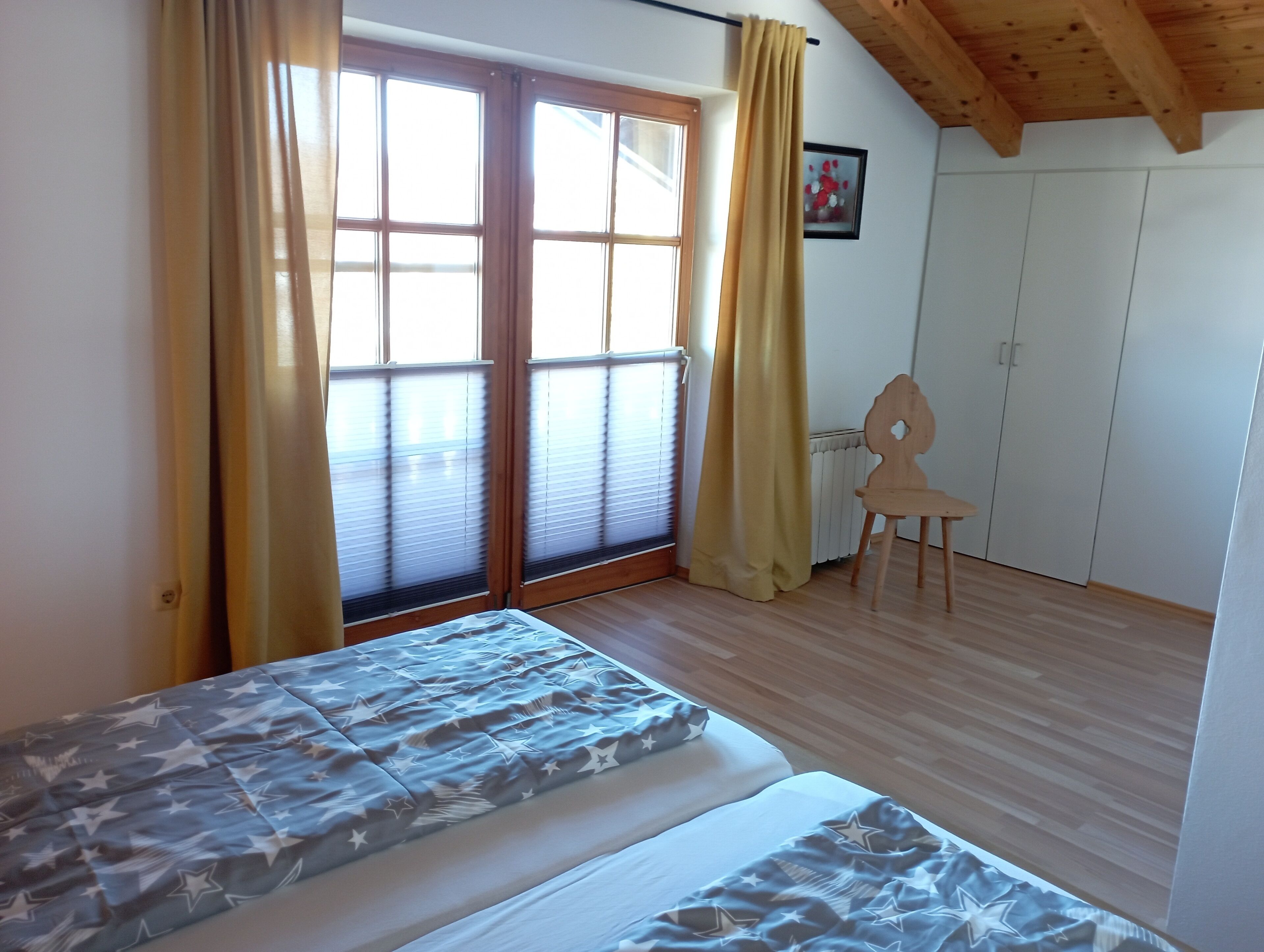 A room with two beds, a chair, a radiator, and a window with curtains.
