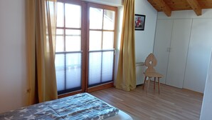 Ein Zimmer mit zwei Betten, einem Sessel, einem Heizkörper und einem Fenster mit Vorhängen.