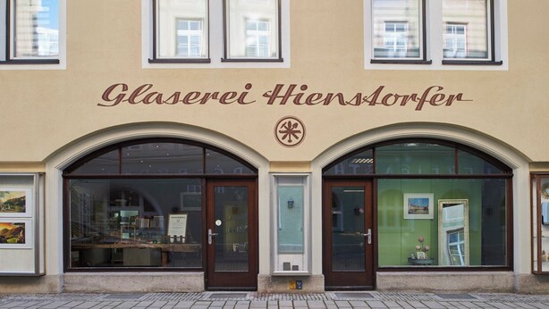 Rakennuksen päällä, sisäänkäynnin yläpuolella, on kyltti, jossa lukee: ”Glaserei Hiansdorfer”.