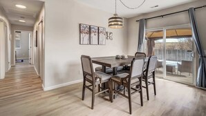A dining area with a wooden table and chairs, a hanging light fixture, and a view through a glass door to an outdoor patio.