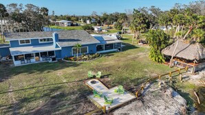 A large house with a covered patio, a swimming pool, and a thatched-roof structure. - Riverside Oasis! Home w/ Tiki Hut & Firepit (Bradenton)