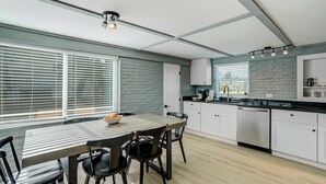 A modern kitchen with white cabinets, a black countertop, and a dining area with a table and chairs. - Riverside Oasis! Home w/ Tiki Hut & Firepit (Bradenton)