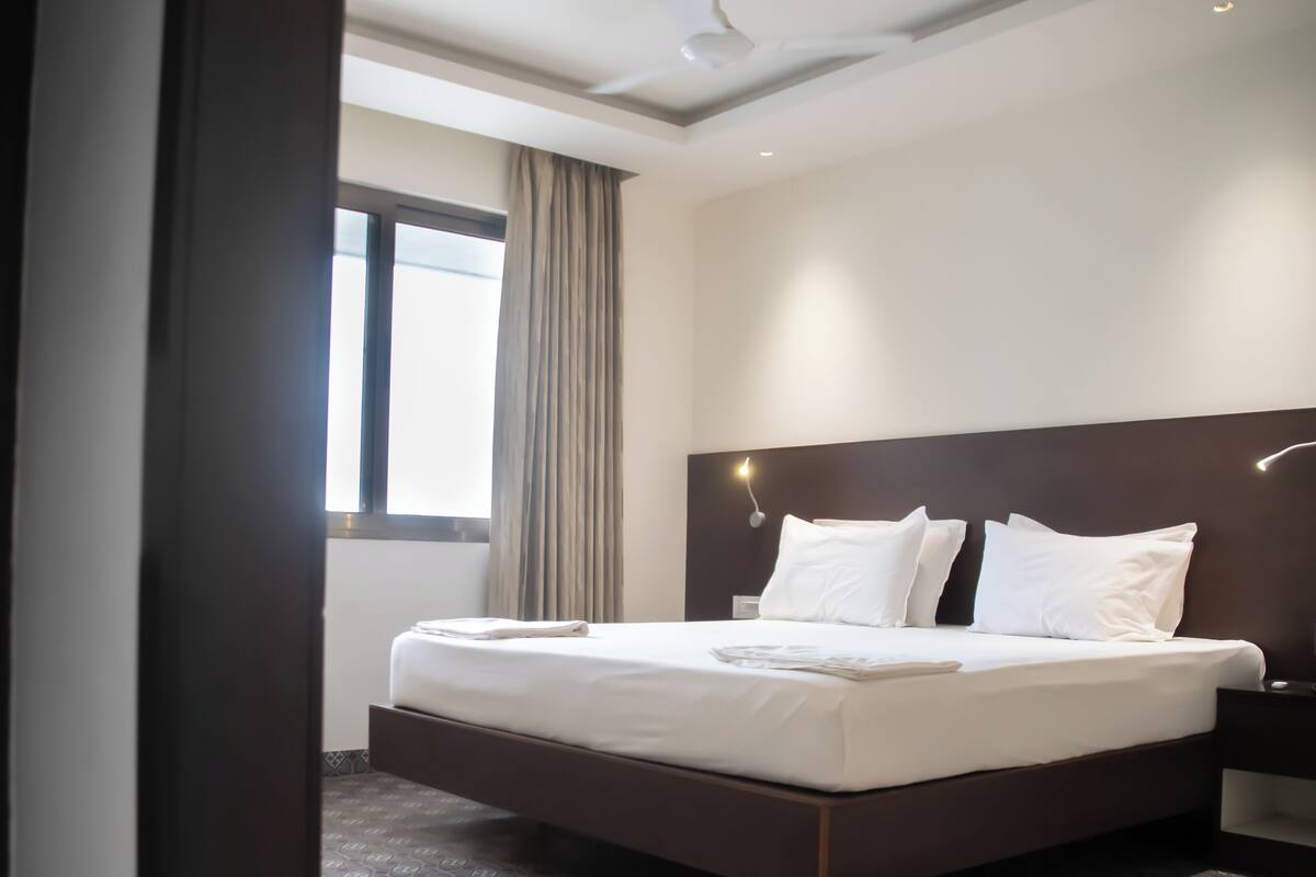 A modern hotel room with a large bed, a nightstand, and a window with curtains.