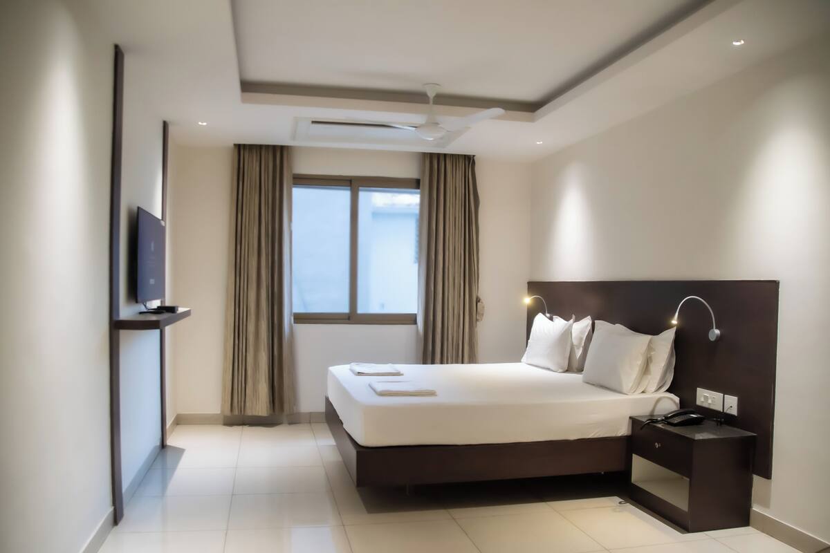 A modern hotel room with a large bed, bedside table, and a flat-screen TV mounted on the wall.