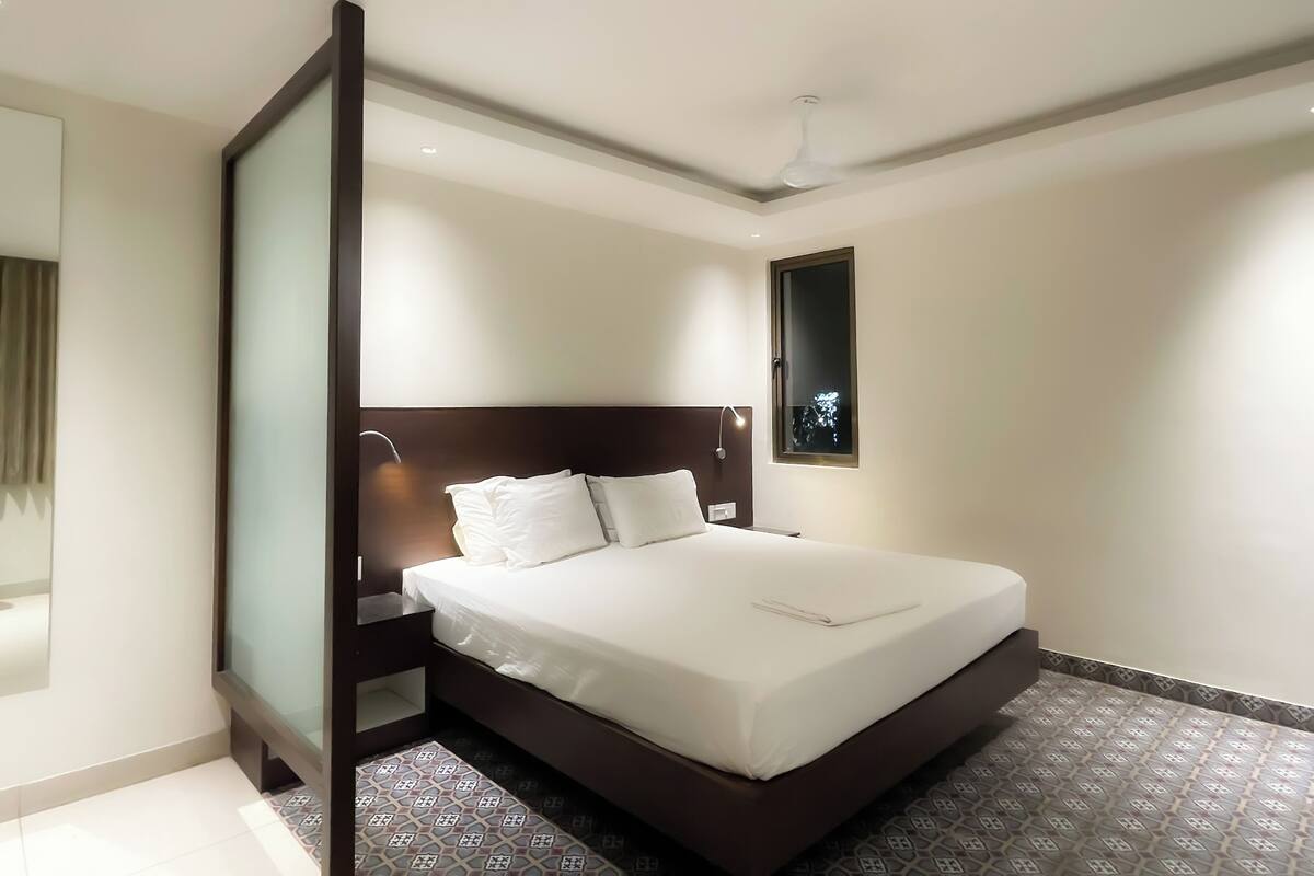 A modern hotel room with a large bed, a nightstand, a bedside lamp, and a window with a view of the night sky.