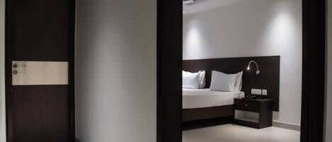 A modern hotel room with a large bed, bedside table, and a dark-colored headboard.