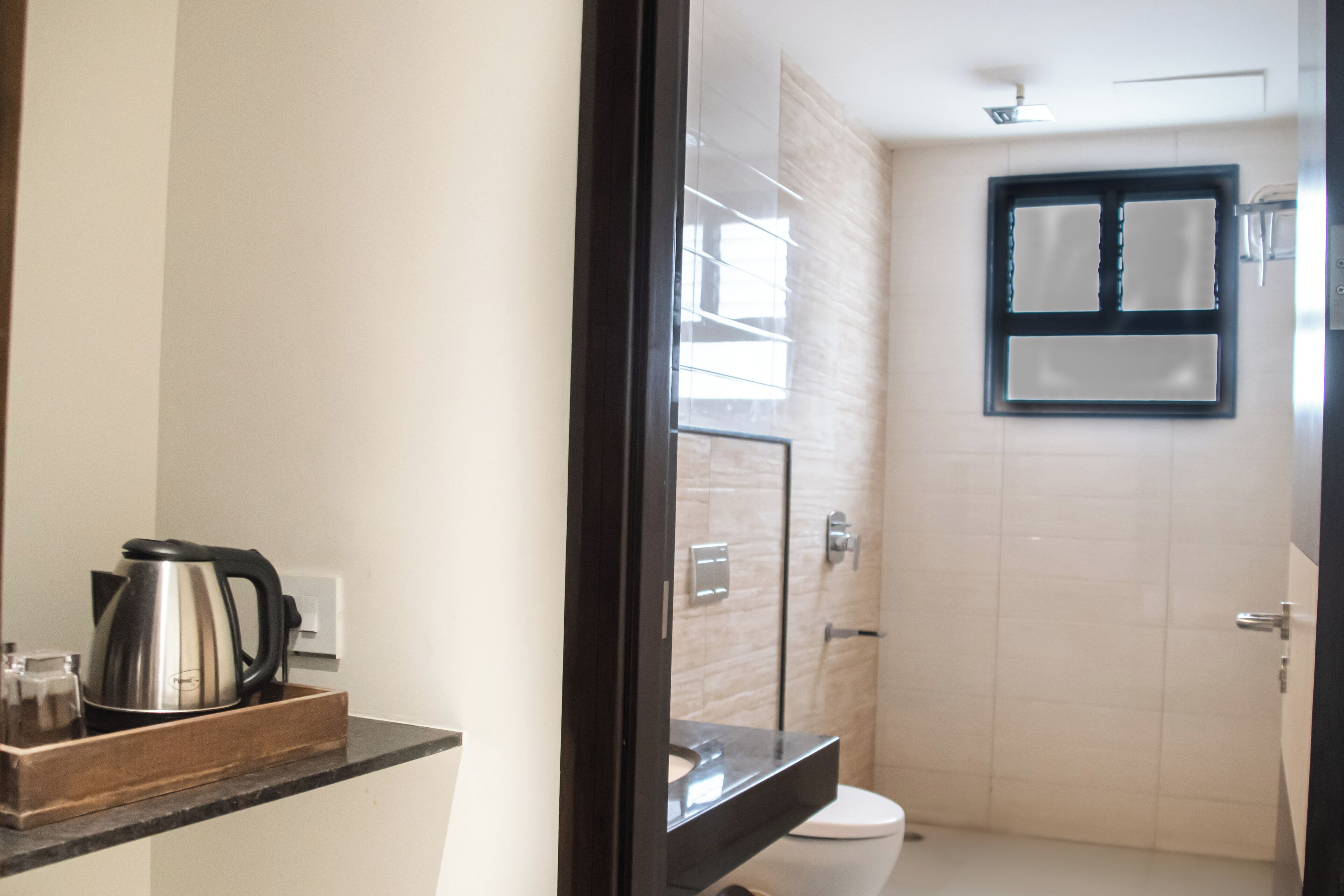 A bathroom with a toilet, a sink, and a shower area. There is a wooden tray with a kettle and glasses on the counter.