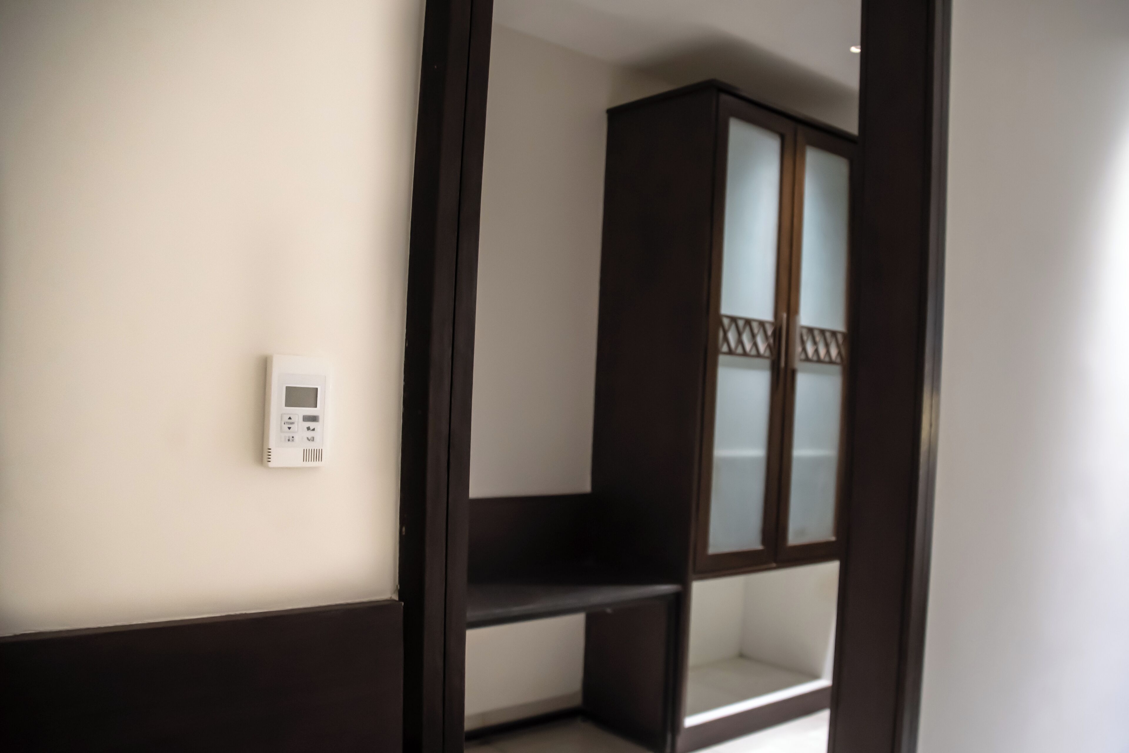 A room with a white wall, a dark wooden cabinet with glass doors, and a thermostat on the wall.