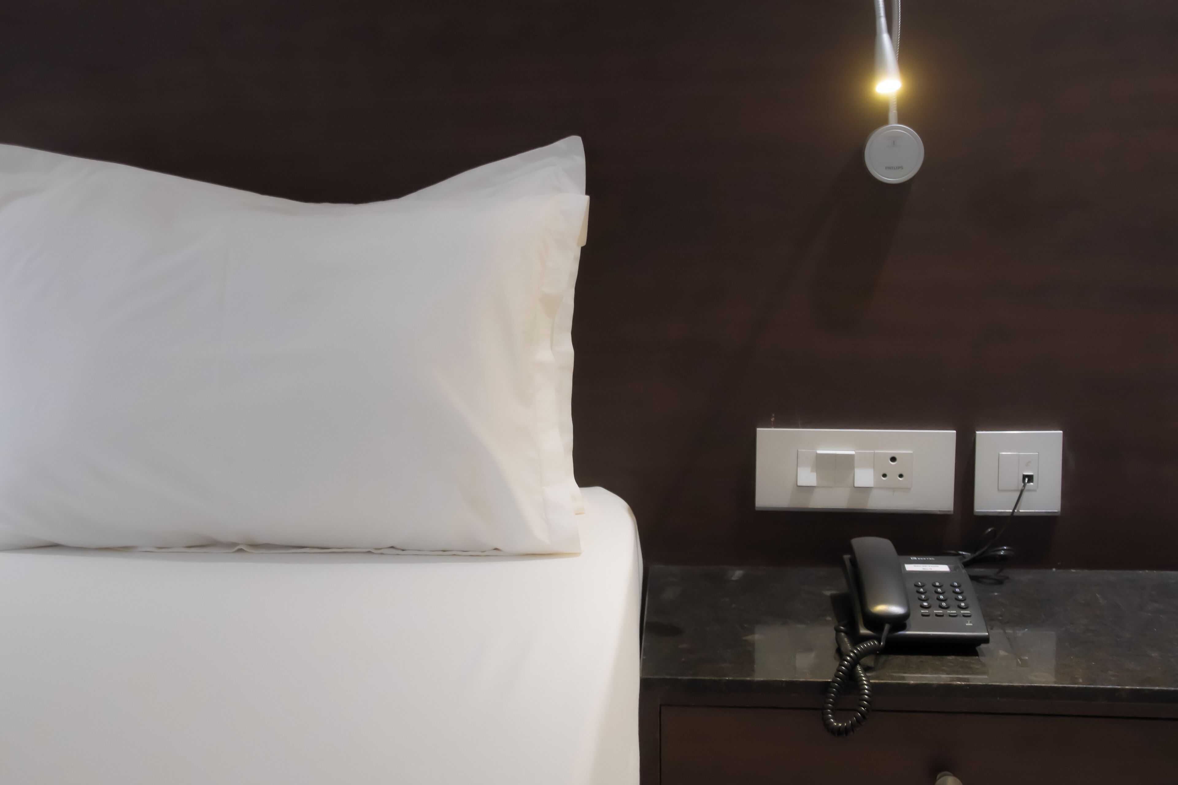 Een hotelkamer met een bed, een bedtelefoon en een stopcontact.
