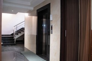 Un ascensor moderno con pantalla digital, una escalera con barandillas de metal y un suelo de mármol.