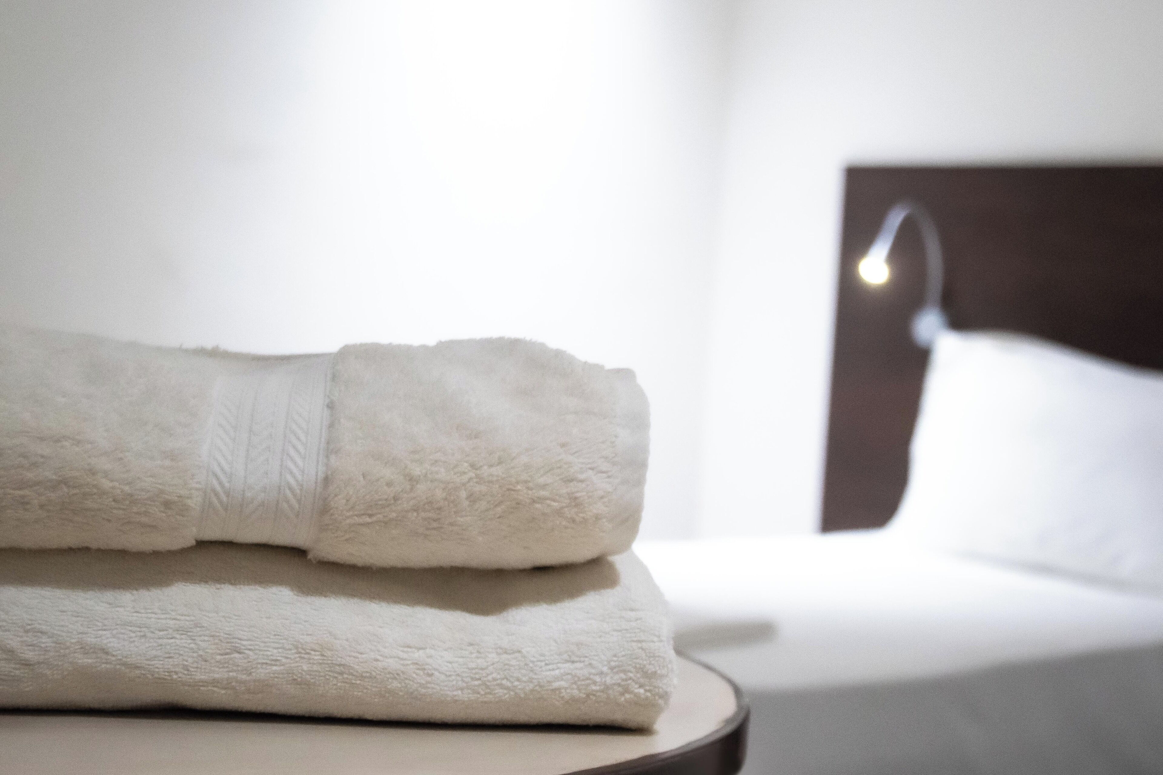 Un asciugamano bianco piegato ordinatamente su un tavolo rotondo in una stanza d'albergo, con un letto sullo sfondo.