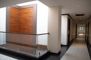 A modern hotel corridor with a glass railing, wooden panel wall, and a long, narrow hallway with doors on one side. - SV Grand (Mettupalayam)