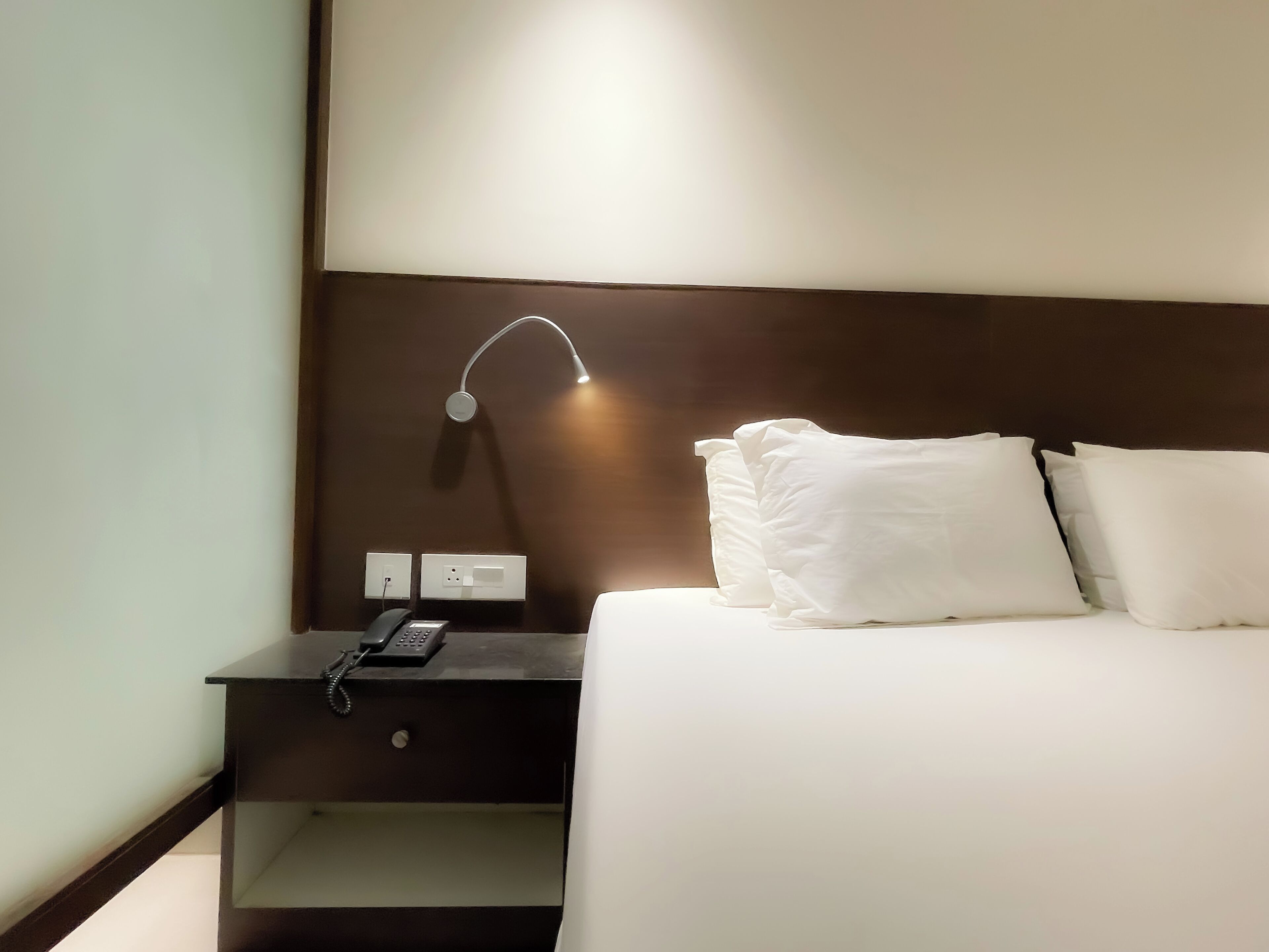 Et hotelværelse med en pænt redt seng, et natbord med lampe og en telefon.