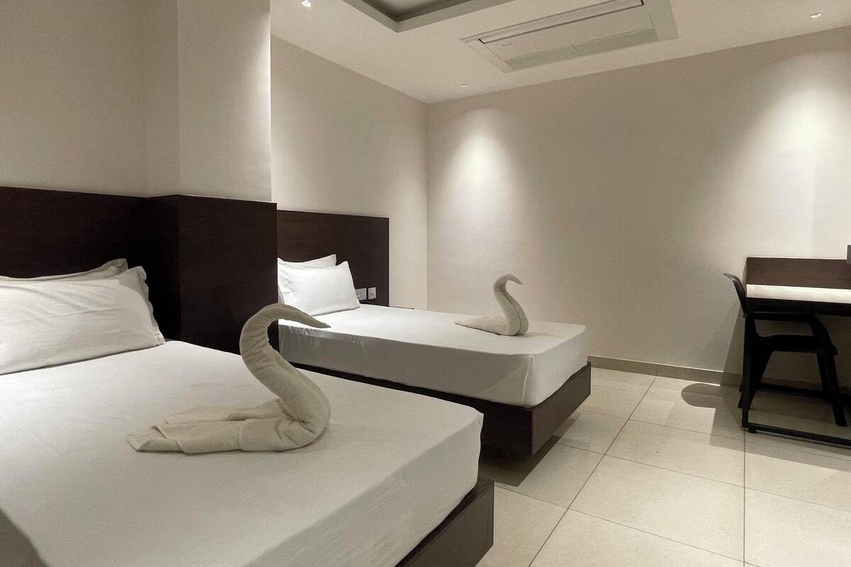 A hotel room with two beds, each with a swan-shaped towel. There is a desk and chair in the room.
