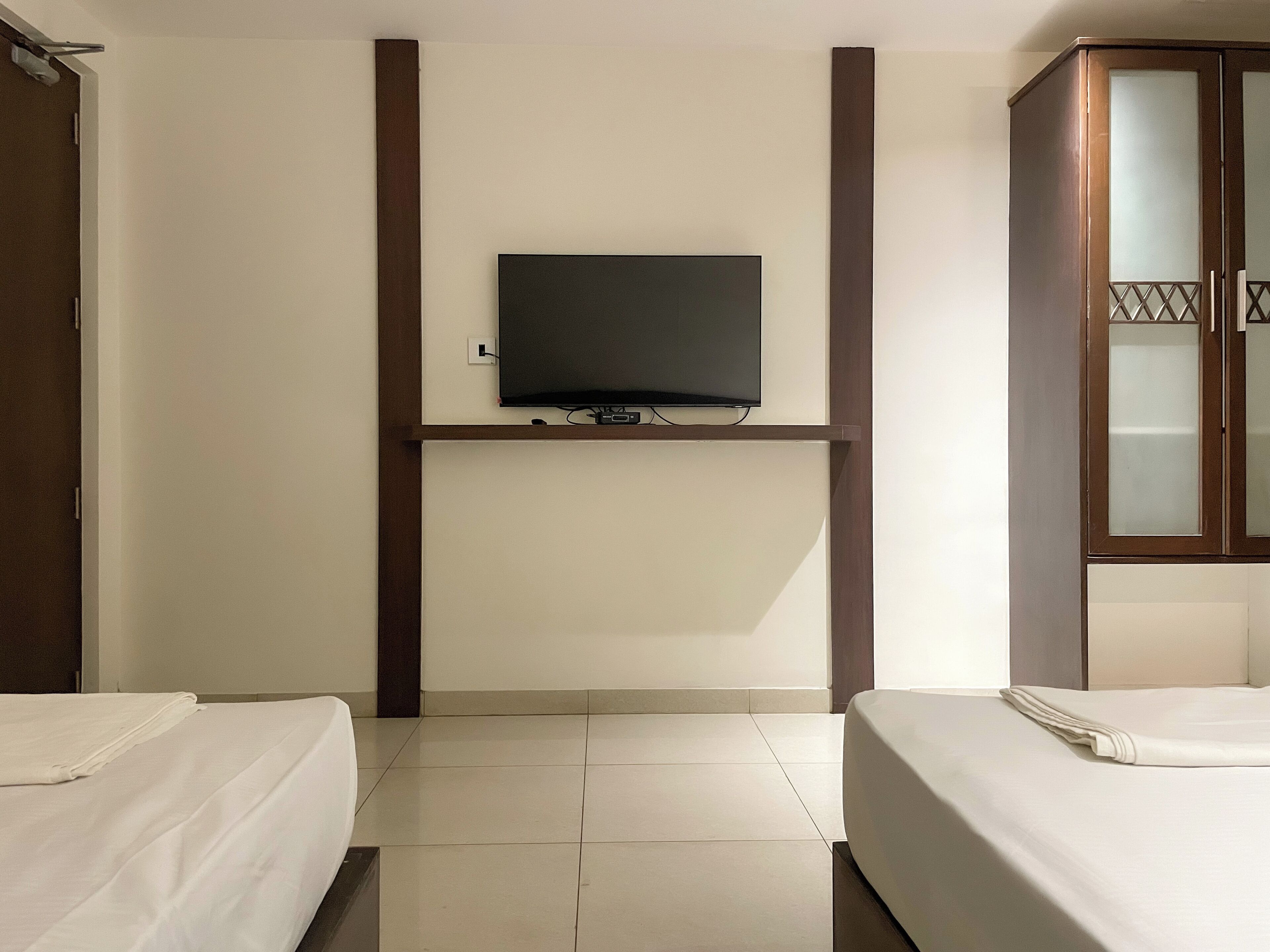 Habitación de hotel con dos camas, un televisor montado en la pared y un armario de madera.