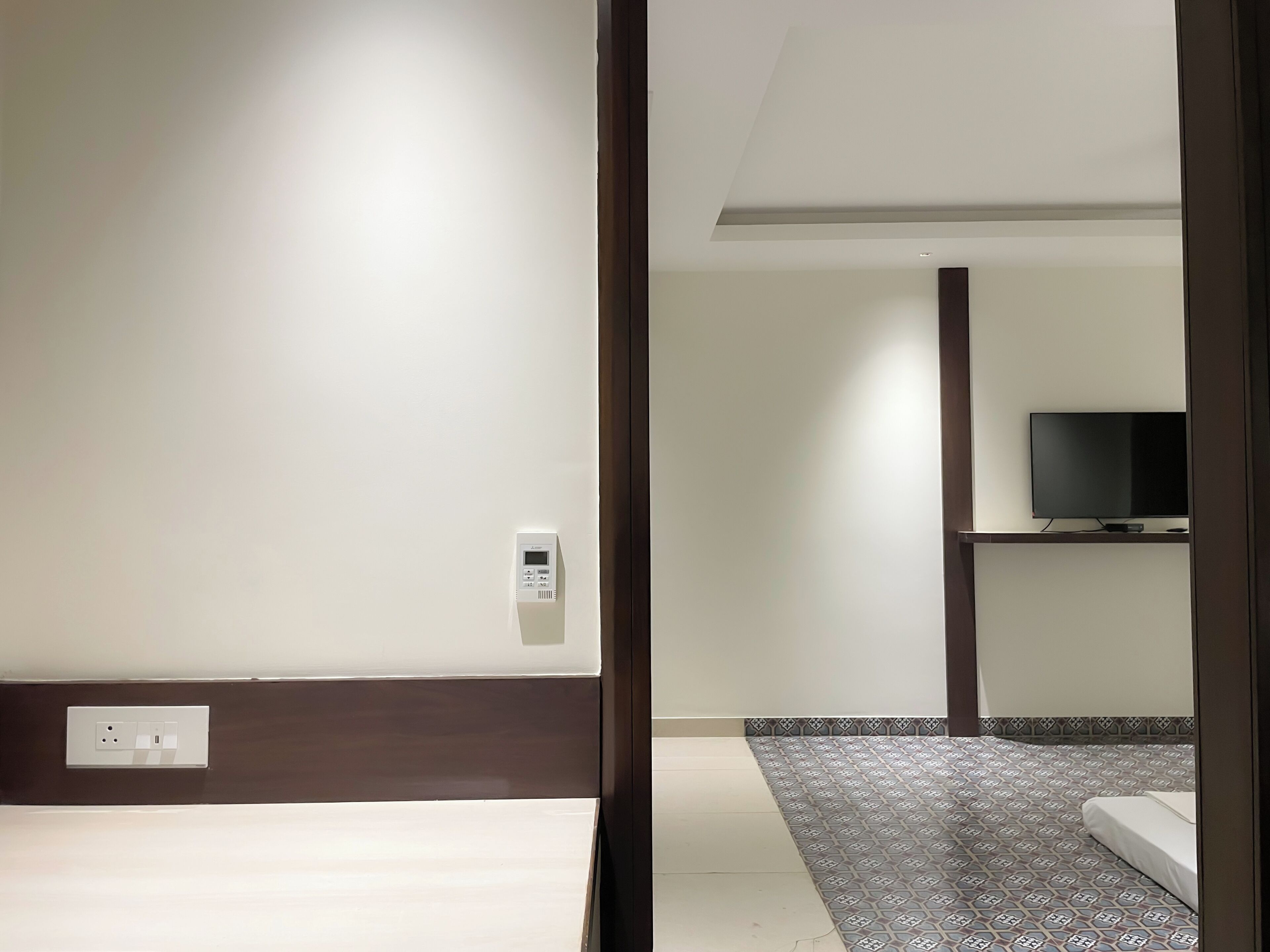 Una habitación de hotel con cama, televisor sobre un soporte y panel de control en la pared.