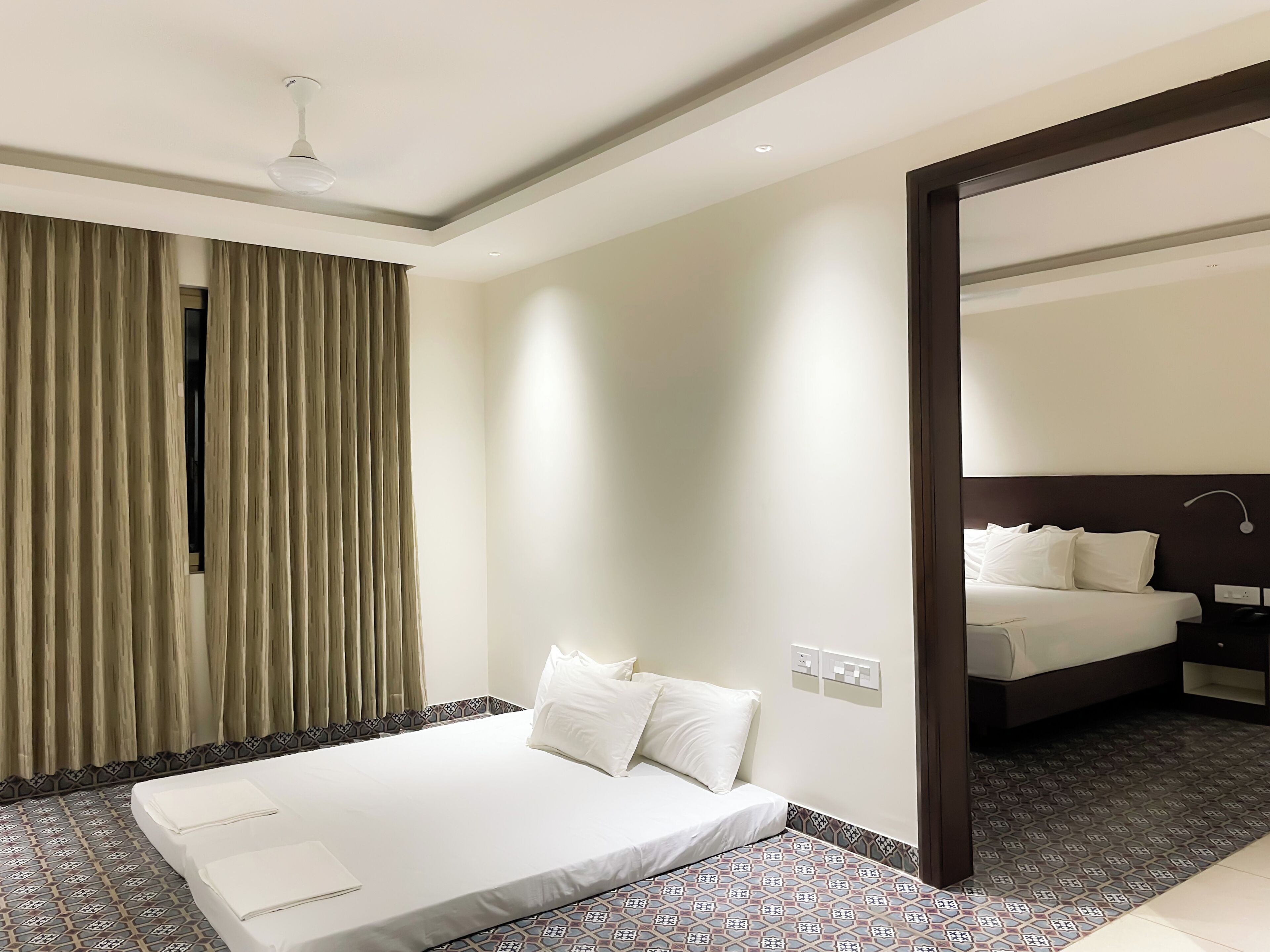 Habitación de hotel con cama, espejo, ventilador de techo y suelo estampado.