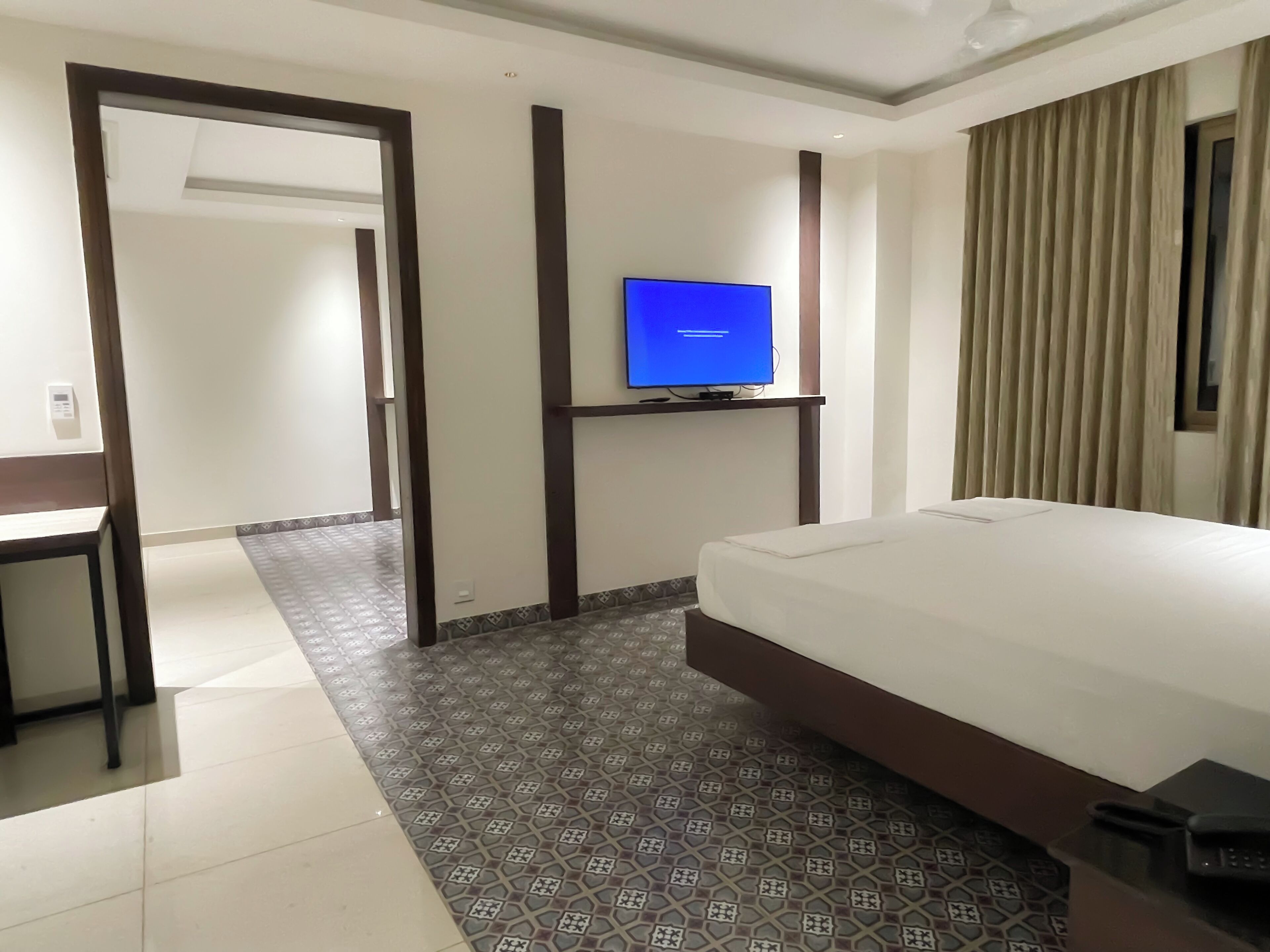 Une chambre d’hôtel avec un lit, un bureau, un téléviseur fixé au mur et un sol à motifs.