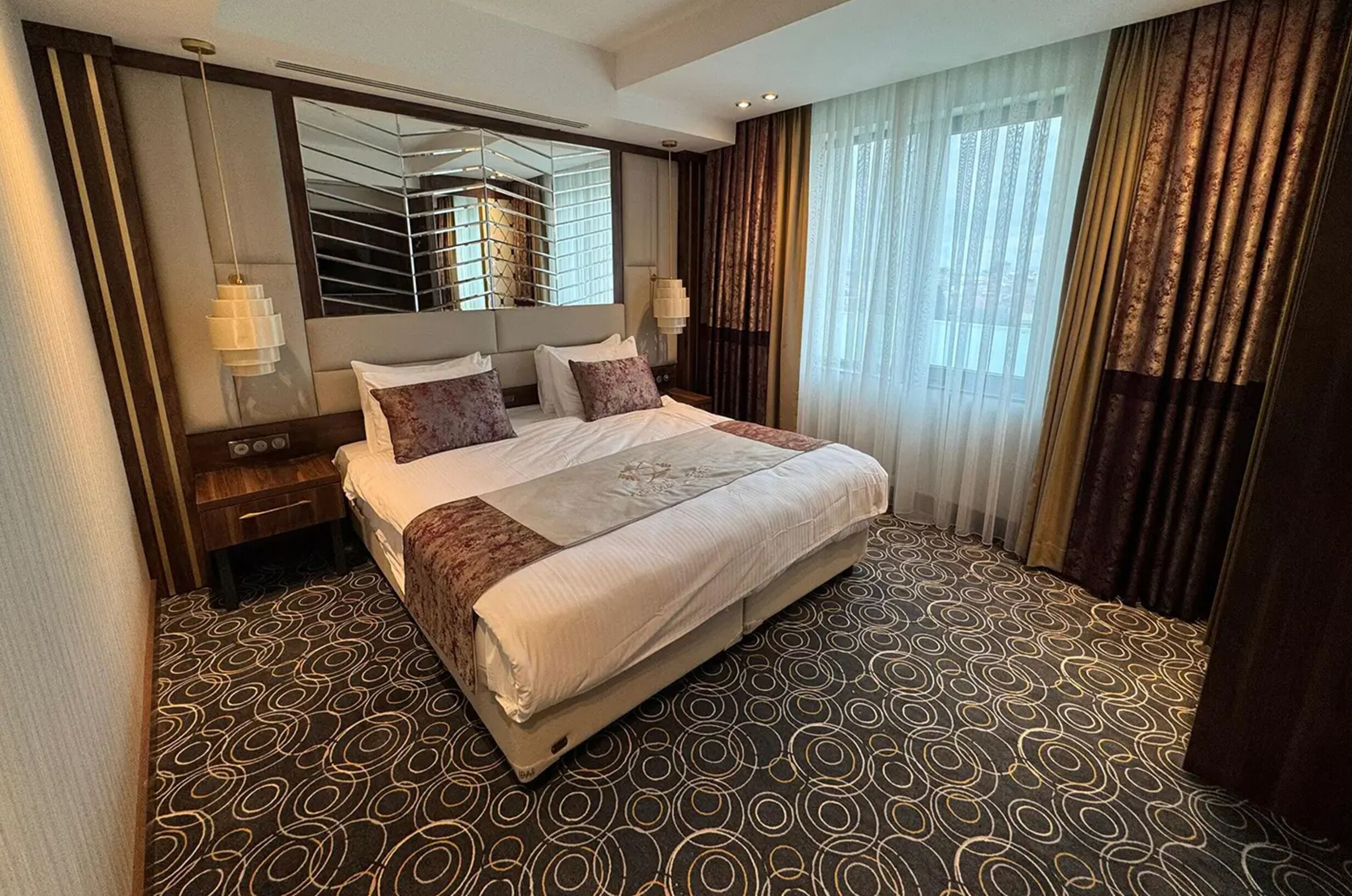 Een hotelkamer met een groot bed, een spiegel, een nachtkastje en een kamerbreed tapijt met dessin.
