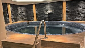 Un jacuzzi con una escalera de metal, rodeado de escalones de madera y un muro de piedra.