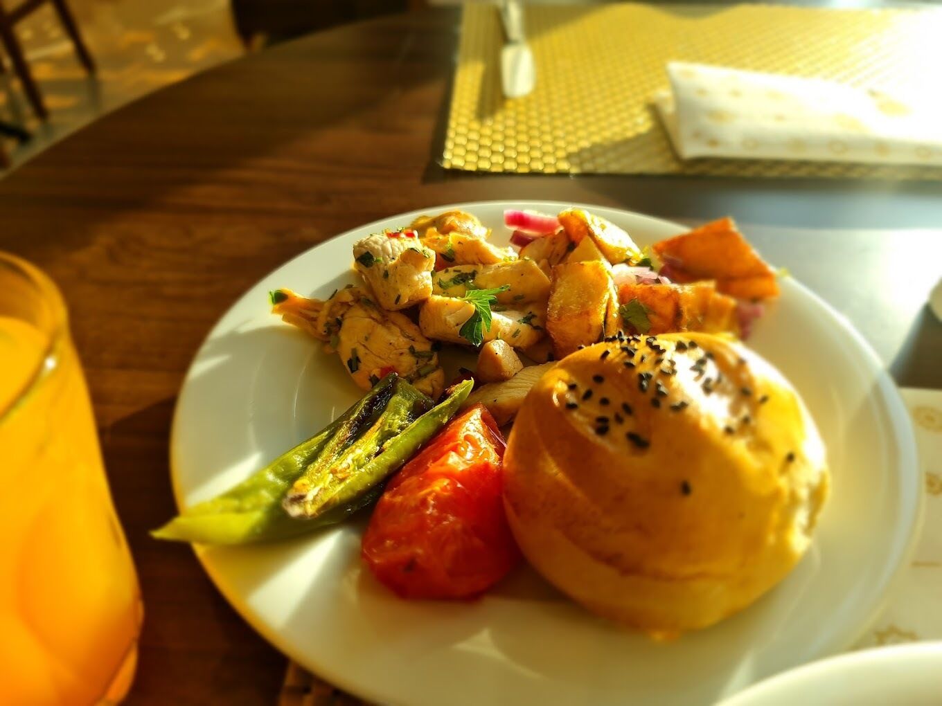 A plate of food with grilled vegetables and a bun on a wooden table.