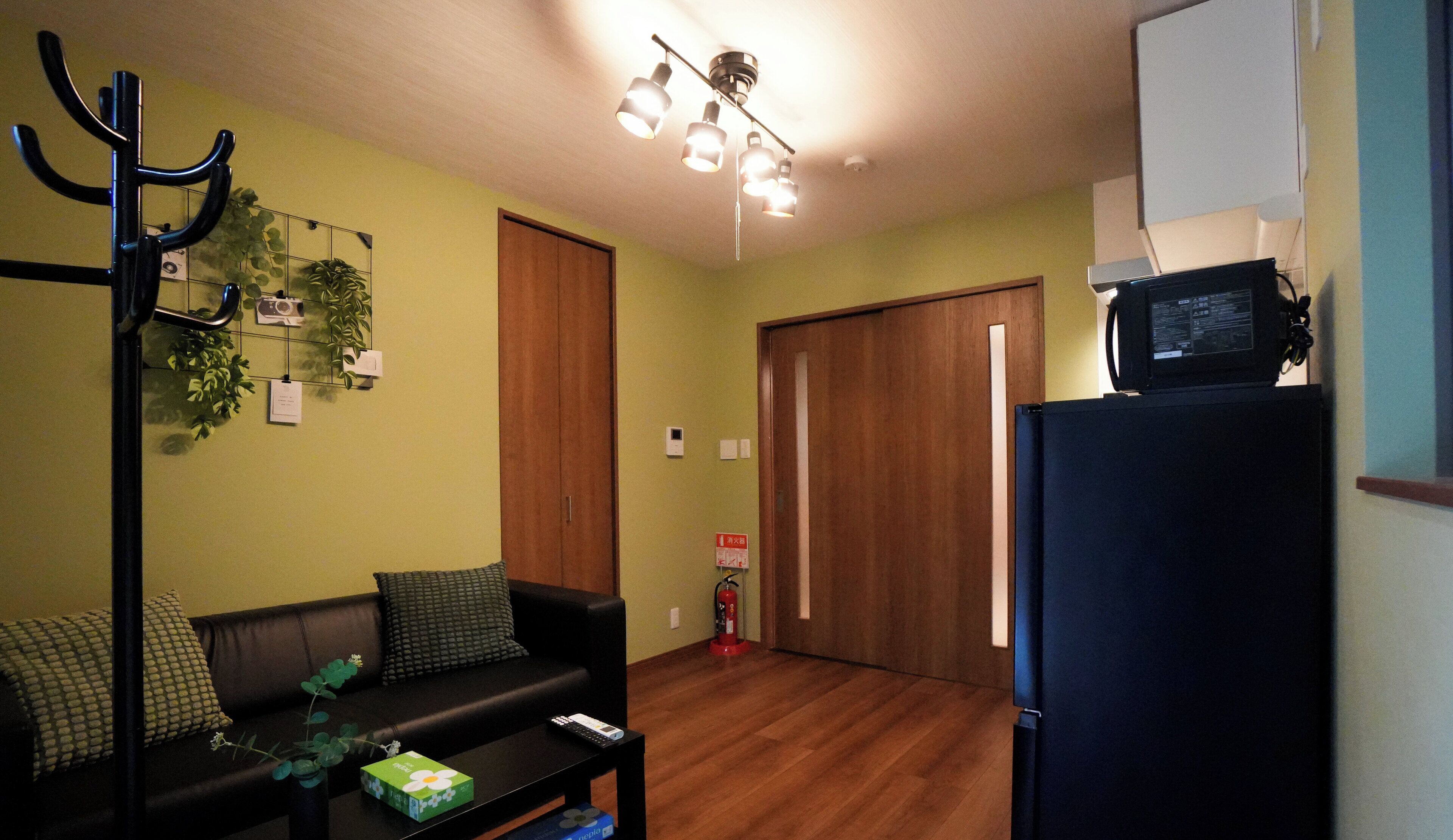 Een woonkamer met een zwarte bank, een salontafel, een zwarte tv-kast, een plafondlamp en een houten deur.