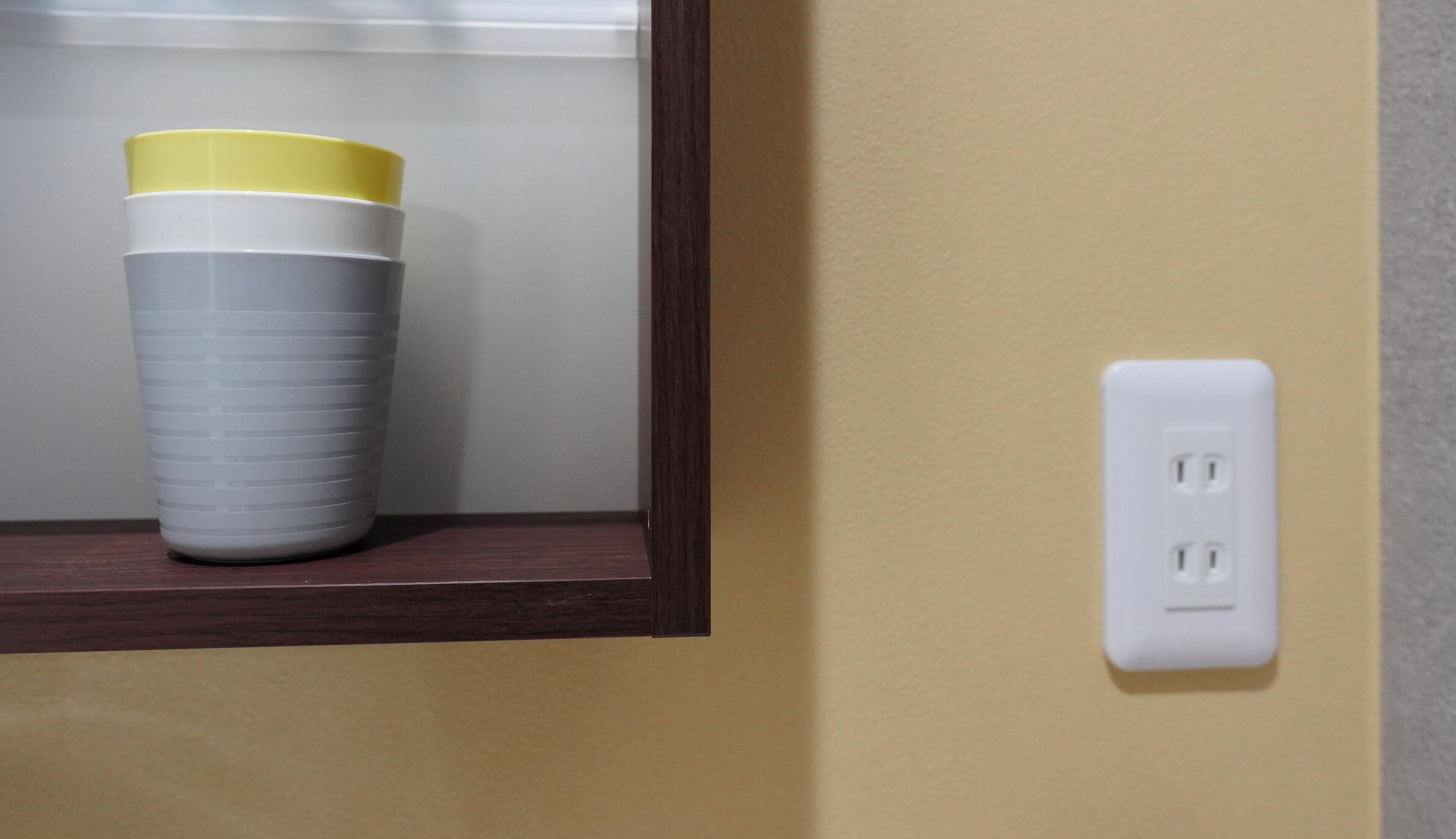 A wall with a power outlet and a shelf with a cup.