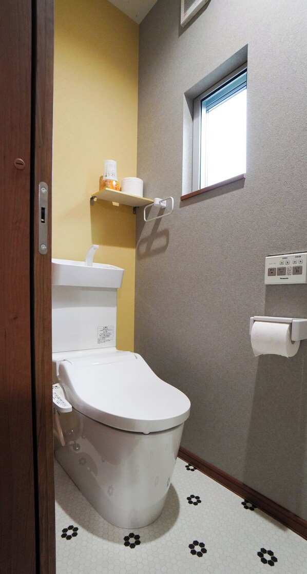A bathroom with a toilet, a shelf with toiletries, a window, and a toilet paper holder. - HANASTAY TSUBAKI (Osaka)