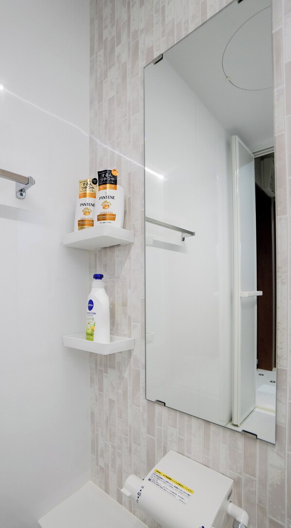 A bathroom with a large mirror, a toilet, and shelves holding toiletries. - HANASTAY TSUBAKI (Osaka)