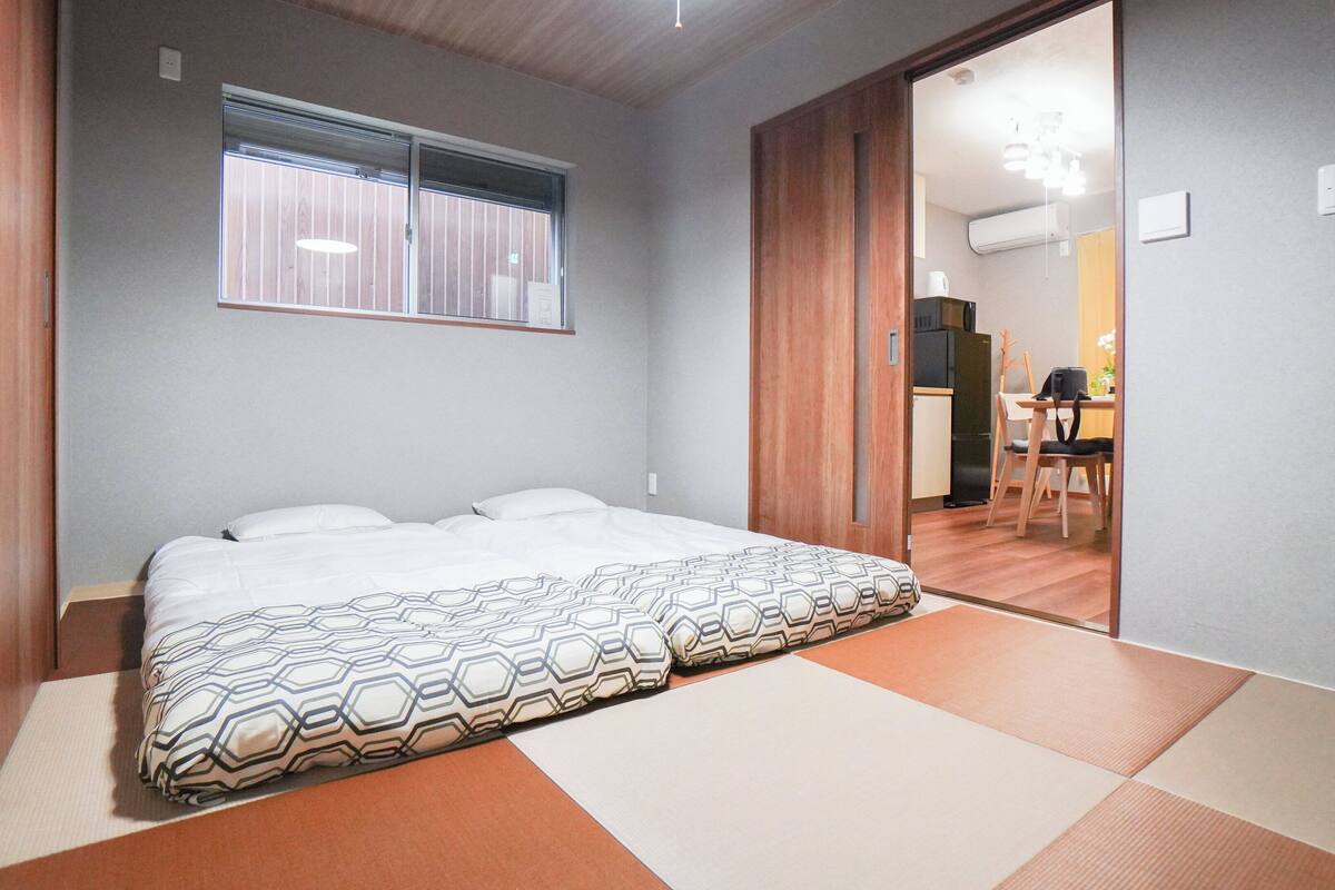 A bedroom with a bed, a window, and a sliding door leading to a kitchen area.