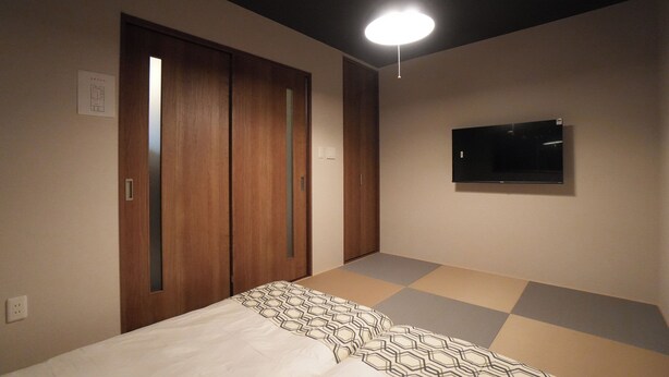 Ein Schlafzimmer mit einem Bett, einem an der Wand montierten Fernseher und einem Kleiderschrank mit Schiebetüren.