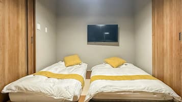Une chambre avec deux lits, un luminaire au plafond et un téléviseur à écran plat fixé au mur.