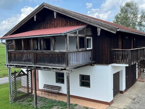 Stunning two-story building with a spacious balcony and a bench on the ground level, set amidst a serene grassy field.