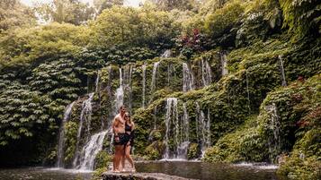 Un couple se tient sur un rocher, près d’une cascade, dans une forêt luxuriante et verdoyante.