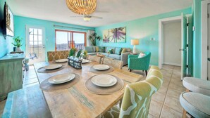A dining area with a wooden table set for four, a sofa, and a chair. - Sleeps 18, 2 Condos | Beach Access, Pool, Views, Tennis + Pickleball Courts (Port Aransas)