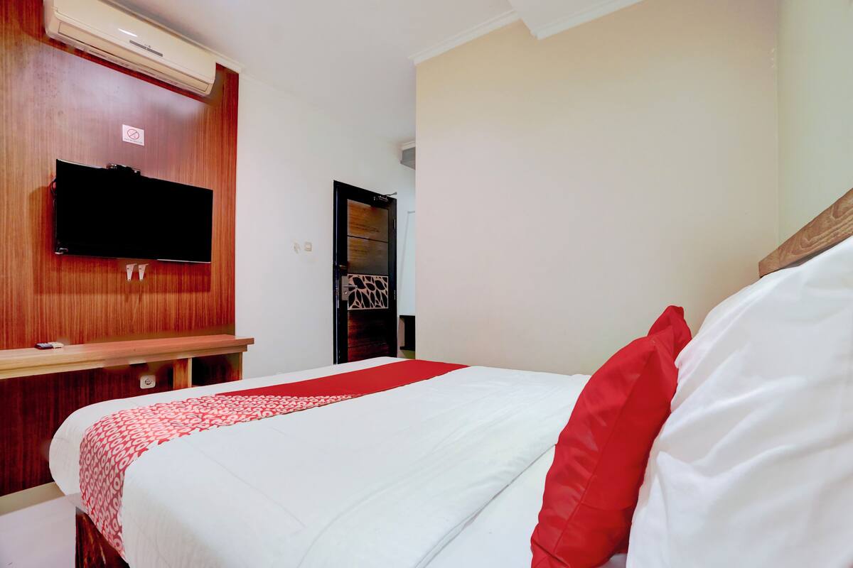 Una habitación de hotel con una cama, un televisor montado en la pared y un escritorio de madera.
