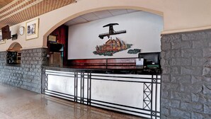 Un área de recepción con una pared de piedra, un reloj, cuadros enmarcados y un emblema decorativo sobre el mostrador.