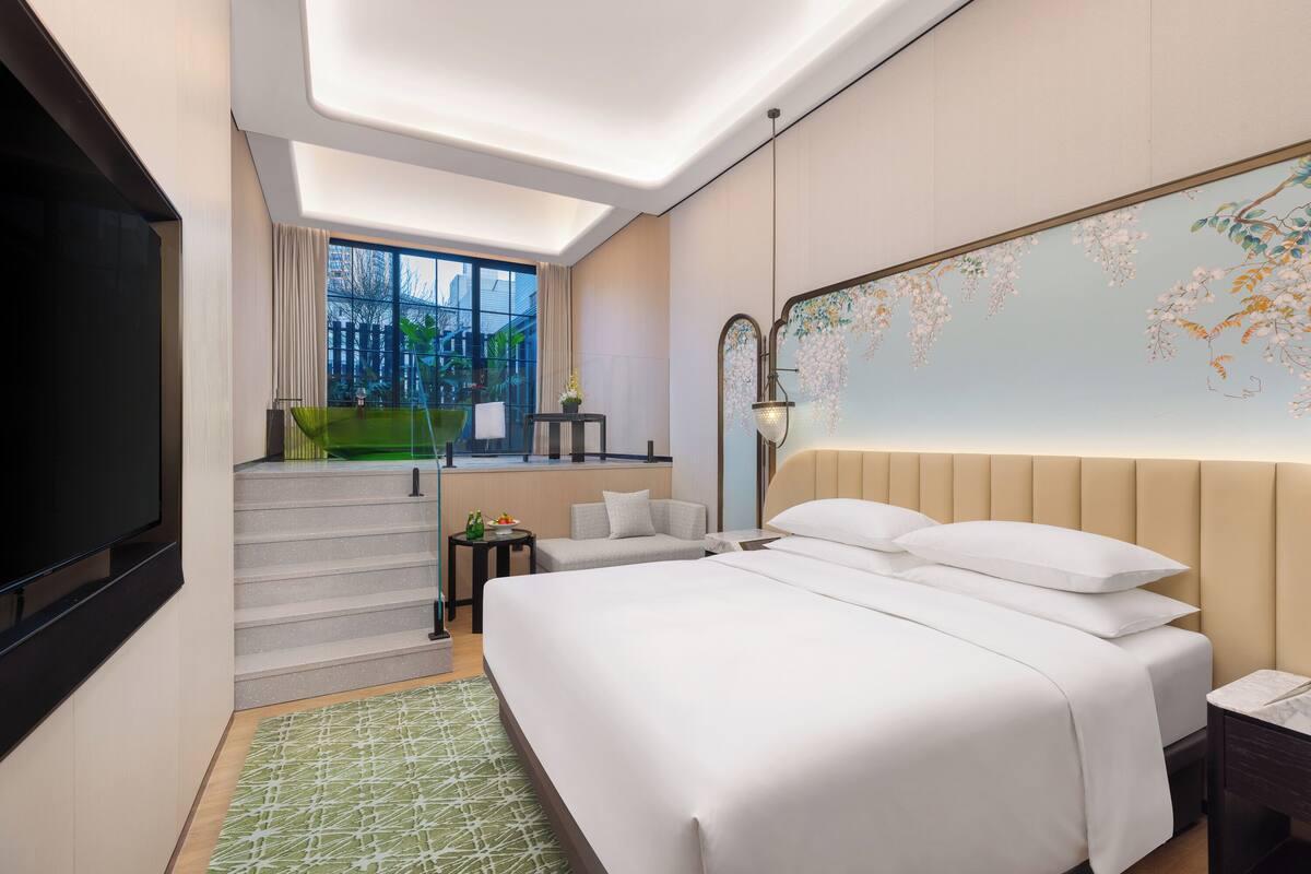 A hotel room with a large bed, a TV, a desk with a chair, and a staircase leading to an outdoor area.