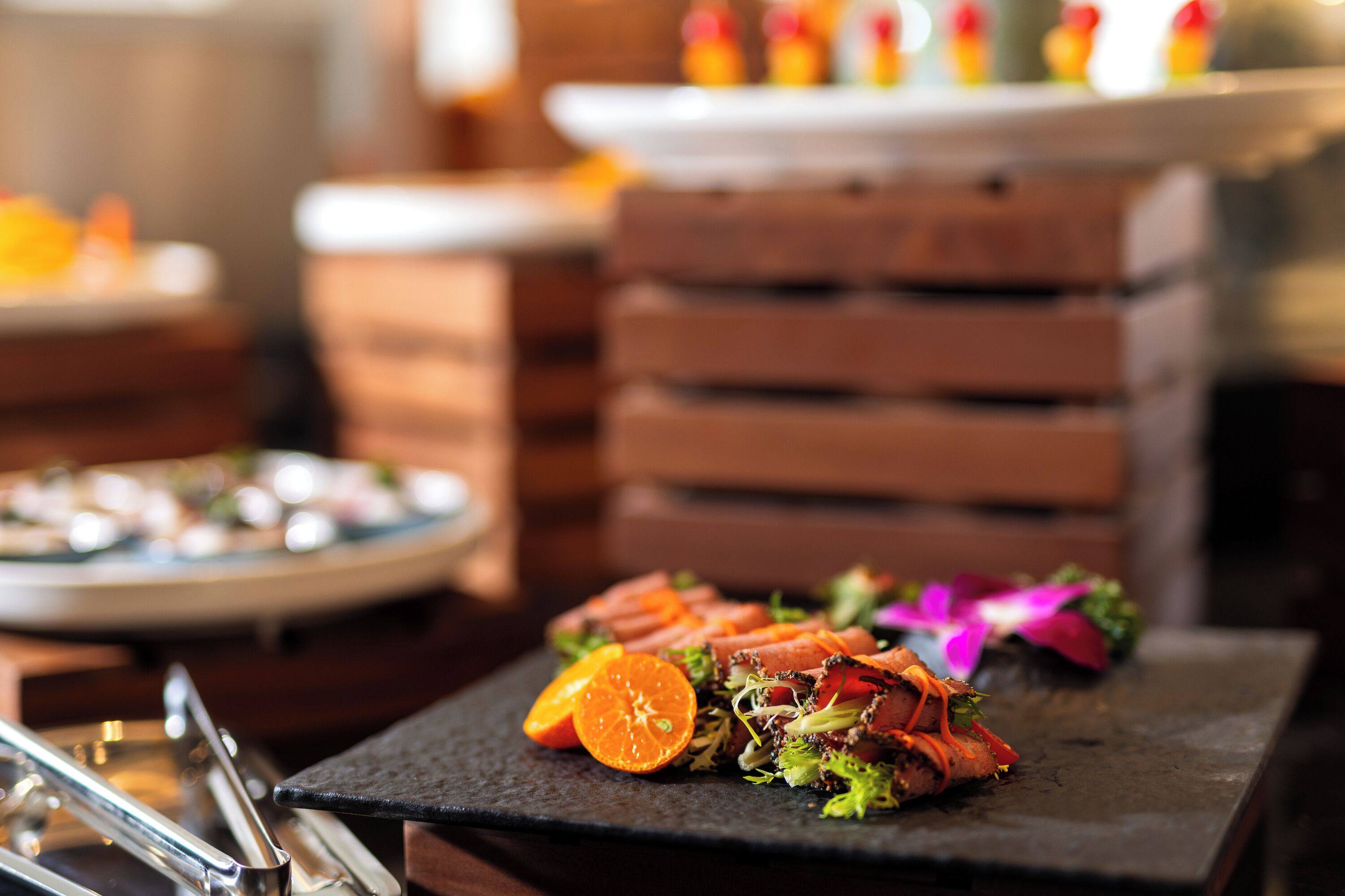 A dining table with a black slate top, a stack of wooden crates, and a plate of food with orange slices and greens.