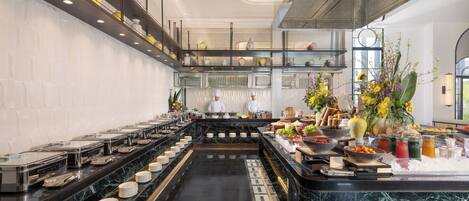 A modern kitchen with marble countertops, a central island with food displays, and a high ceiling with exposed beams.