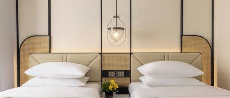 A hotel room with two beds, a nightstand with a clock and a vase of flowers, and a hanging light fixture.