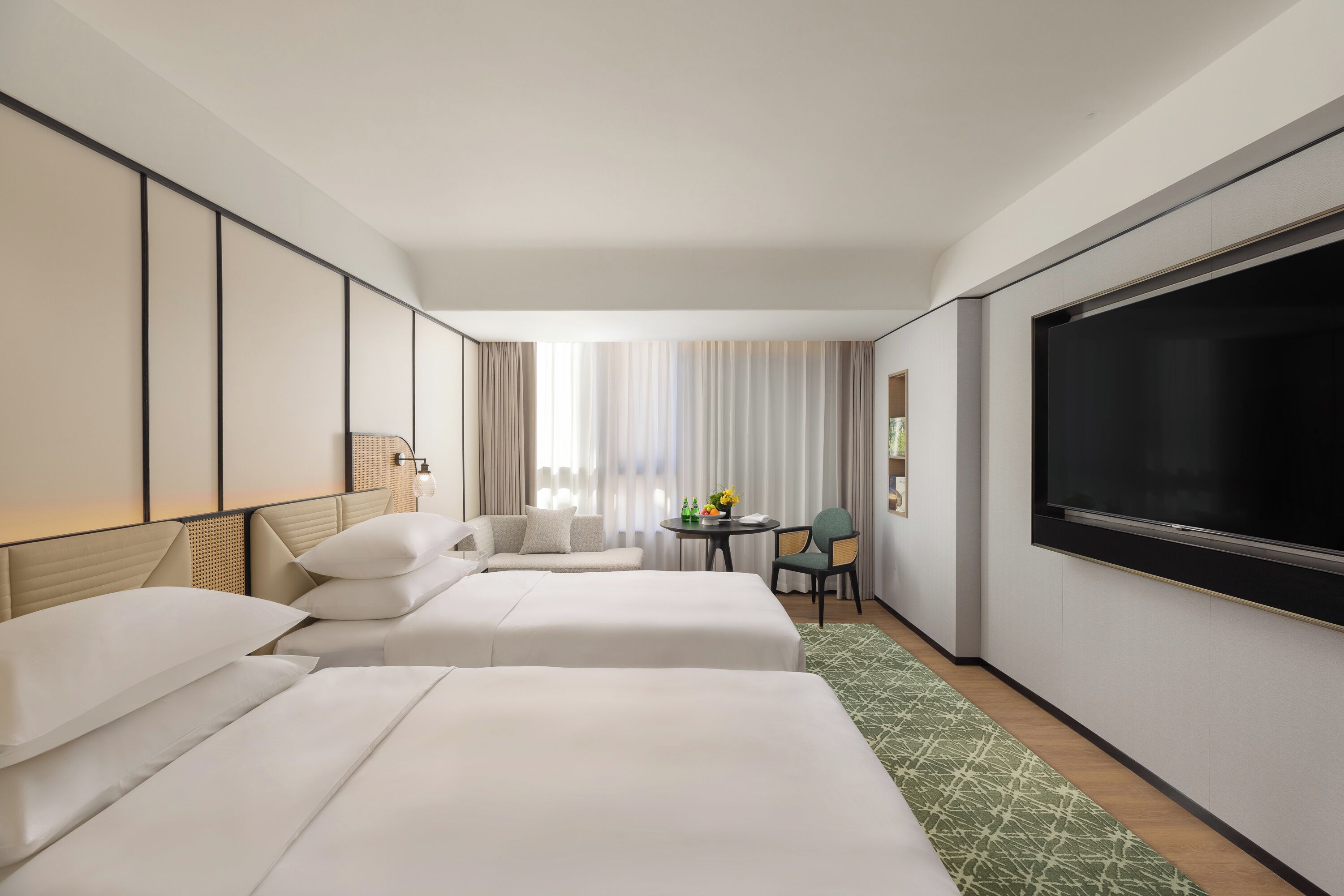 A hotel room with two beds, a seating area with a table, and a large TV screen.