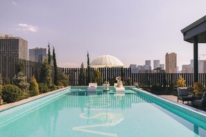 Enjoy a refreshing swim with a city view from our rooftop pool, surrounded by lounge chairs and a shaded area.